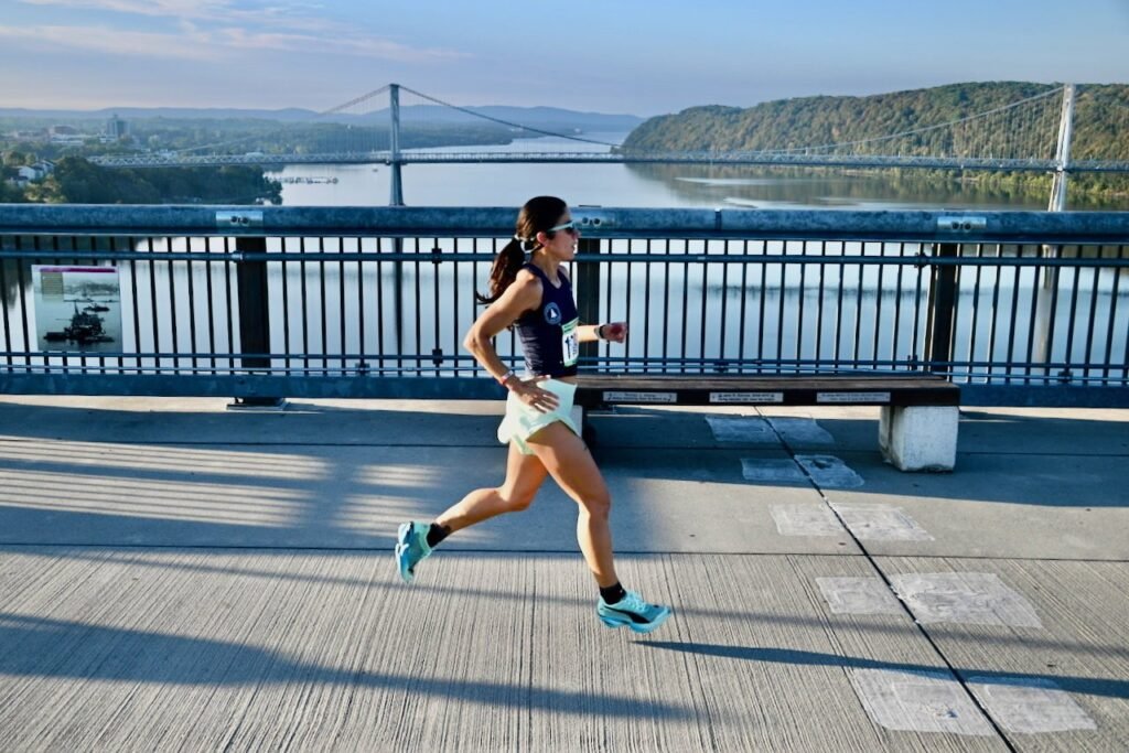 A Hudson Valley Track Club runner on the Walkway Over the Hudson, with the Mid-Hudson Bridge behind